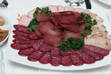 Dish with delicious sliced salami, slices of ham, sausage, beef tongue, parsley. Meat dish with selection.