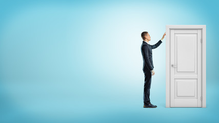 Fototapeta premium A businessman on blue background touches a white doorframe with a closed door inside.