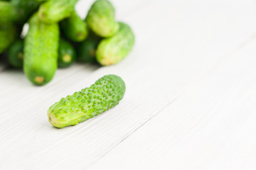 Single cucumber and heap of green fresh cucumbers on white rustic background