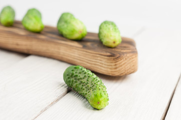 Many fresh green cucumbers on rustic cutting board and one single cucumber on old white wooden planks