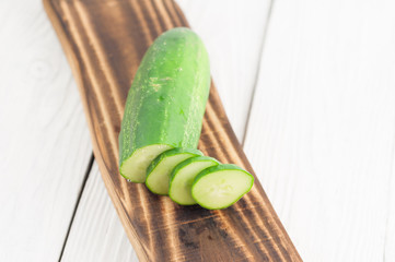 Chopped fresh green cucumber on rustic brown cutting board on old white wooden planks