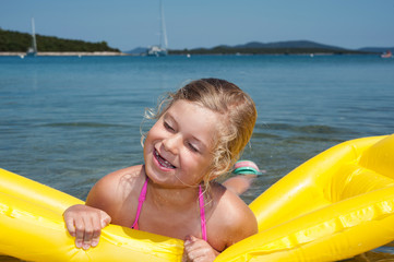 little girl is swimming with air mattress in blue sea