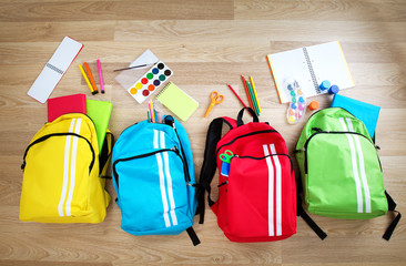Colourful children schoolbags on wooden floor. Backpacks with school accessories