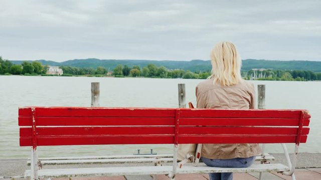A woman sits on a red bench, admiring the view of the lake. Back view. Rest on Lake Balaton in Hungary