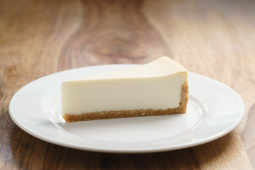 slice of traditional new york cheesecake on white plate on wood table