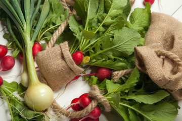 Fresh organic red radishes with tops and green leaves on white wooden background. Top view....
