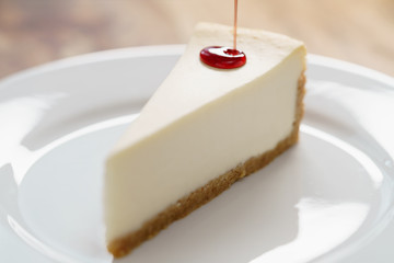 pouring berry jam on slice of traditional new york cheesecake on white plate on wood table