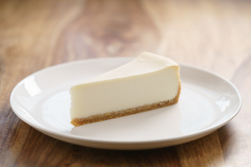 slice of traditional new york cheesecake on white plate on wood table