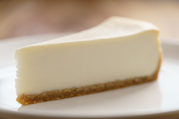 slice of traditional new york cheesecake on white plate on wood table