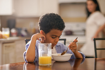 Obraz na płótnie Canvas cute little boy eating breakfast with mother behind him