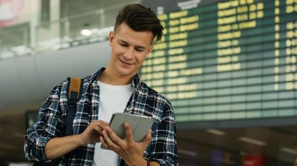 Attractive smiling man in casual shirt using tablet for checking the ticket on the arrivals table background. Close up shot.
