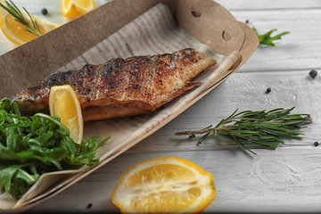 Cardboard box with delicious fish and arugula on table