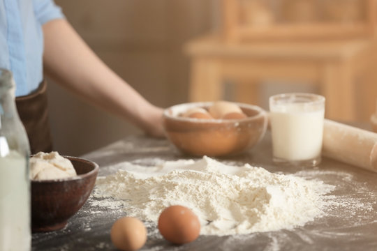 Female chef with flour and ingredients for dough on table in kitchen