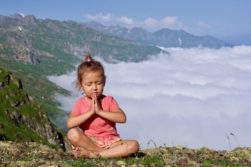Little cute girl meditating on top of mountain