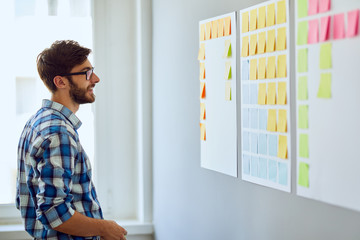 Young start-up businessman looking for inspiration on wall with post-it notes