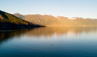 Fototapeta premium Aerial shot of kayaker on lake with mountains while sunset