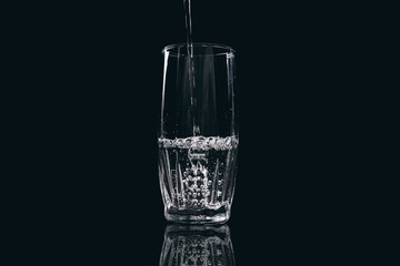 Water is poured into a glass on a black background