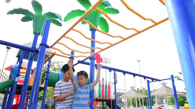 Happy Young asian boy hang the yellow bar by his hand to exercise at out door playground under the strong sunlight in summer time.