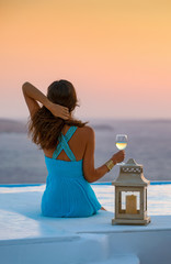 Elegante Frau in blauem Kleid sitzt am Rand des Pools und genießt den Sonnenuntergang