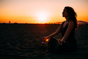 Yoga in the beach. Woman meditating in lotus pose at sunset. Low light photo.