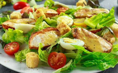 Fresh healthy Caesar salad with chicken, egg quail, tomatoes, Cheese and Croutons in a white plate