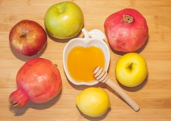 Beautiful green, yellow and red apples, pomegranates and lemons with honey on a wooden background. The traditional Jewish holiday Rosh HaShanah (Jewish New Year) concept. 