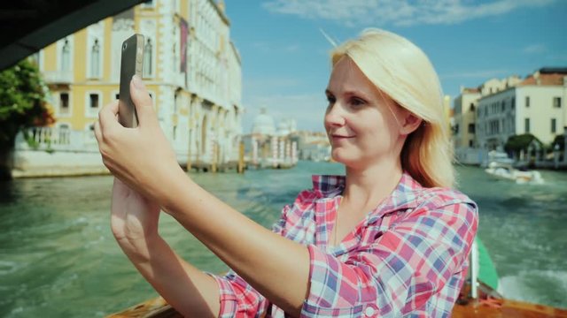 Young woman takes pictures of beautiful views of Venice in Italy. She sails on a boat on a Grand Canal cruise.