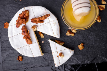Cheese camembert with walnuts and honyey o on black slate plate background. Top view.