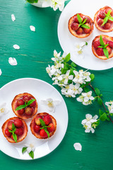 Strawberry tartlet on white plates on green background. Top view.