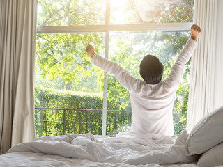 Fototapeta na wymiar lazy man happy waking up in the bed rising hands to window in the morning with fresh feeling relax