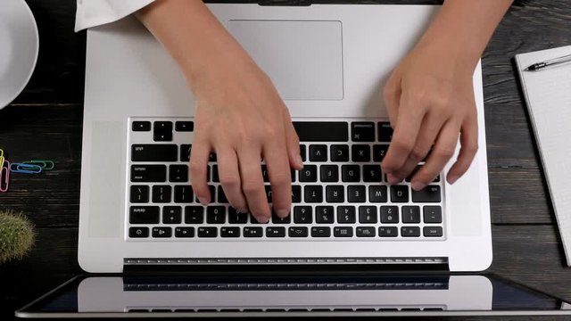 Hands typing at laptop keyboard. Top view, zoom out effect.
