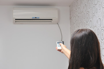 Woman holding remote control in front of air conditioner at home. Woman adjusting temperature in...