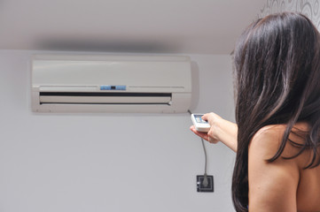 Woman holding remote control in front of air conditioner at home. Woman adjusting temperature in...