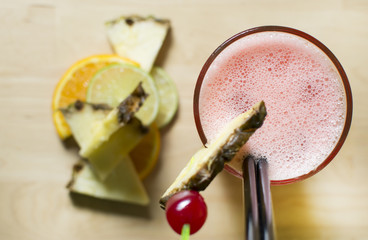Cocktail on a wooden table. Cherry's, lemons, pineapples, and ice.
