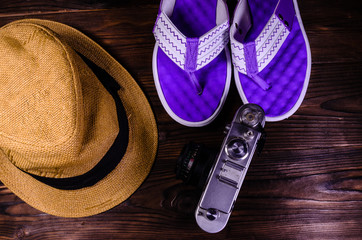 Old rangefinder camera, flip flops and hat on a wooden table. Top view