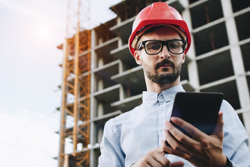 Security inspector with tablet in hand on onstruction site. Businessman builder looks into...