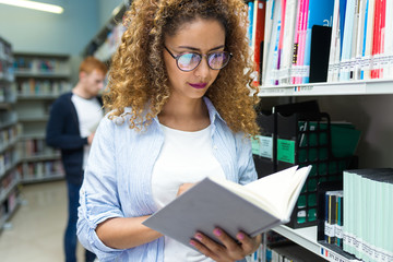 Beautiful young woman consulting a book in a university library.