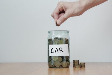 Distribution of cash savings concept. Hand puts coins to the glass money boxes with inscription 'car'.