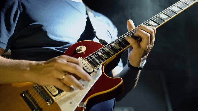 Closeup of man's hands playing electric guitar, smoky scenic