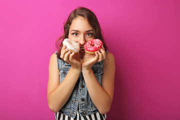 Portrait of young woman with sweet donuts on pink background