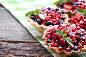 Dessert tartlets with berries and powdered sugar on grey wooden table