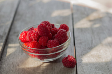 freshly harvested raspberries in a glass bowl on  rustic wooden table