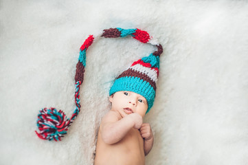 newborn baby in New Year's gnome Cap lays On a white blanket