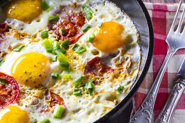 Eggs fried tomatoes in a cast-iron frying pan Wooden vintage background

