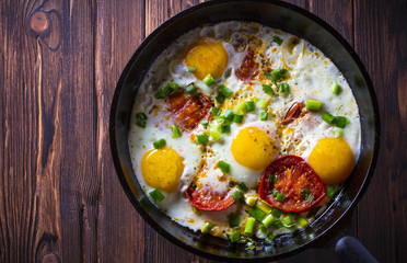 Eggs fried tomatoes in a cast-iron frying pan Wooden vintage background
