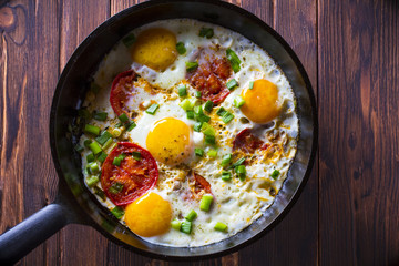 Eggs fried tomatoes in a cast-iron frying pan Wooden vintage background
