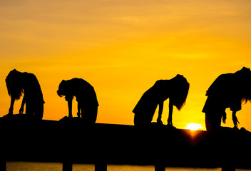 silhouette yoga for woman, group of young woman yoga during sunset with yellow sky, relaxing and happy feeling