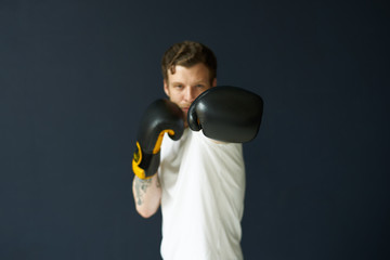 Picture of confident self-determined youg bearded professional kickboxer wearing boxing gloves and sportswear, stretching one arm as if punching invisible enemy. Power and strenght. Selective focus