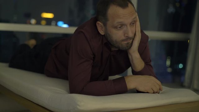 Sad, unhappy man lying on lounger at home at night
