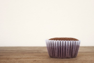 Closeup one homemade chocolate cake on wooden table with white background. Plain cake in white paper baking cup. With copy space.